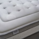 Un matelas avec Âme ressorts ensachés Springsac dont 7 zones de confort. Et tête de lit en tissu gris effet texturé.